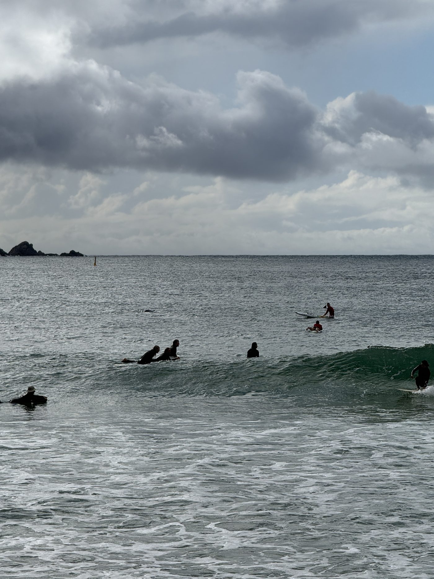 Surfer im Wasser vor Byron Bay unter grauem Wolkenhimmel, eine grüne Welle bricht