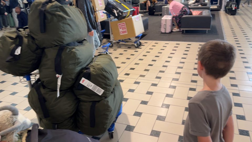 Gepäckwagen voller olivgrüner Seesäcke in der Ankunftshalle des Flughafens Brisbane, daneben Joris im Profil