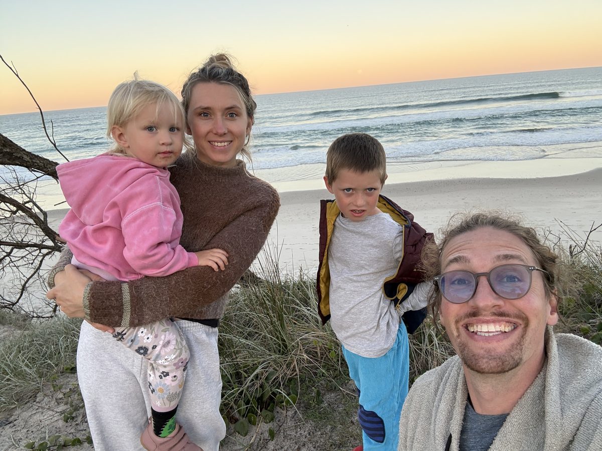 Familien-Selfie am Dünenrand im Abendlicht: Lucy trägt Linnea, Joris und Christian daneben, hinter ihnen Strand und Brandung