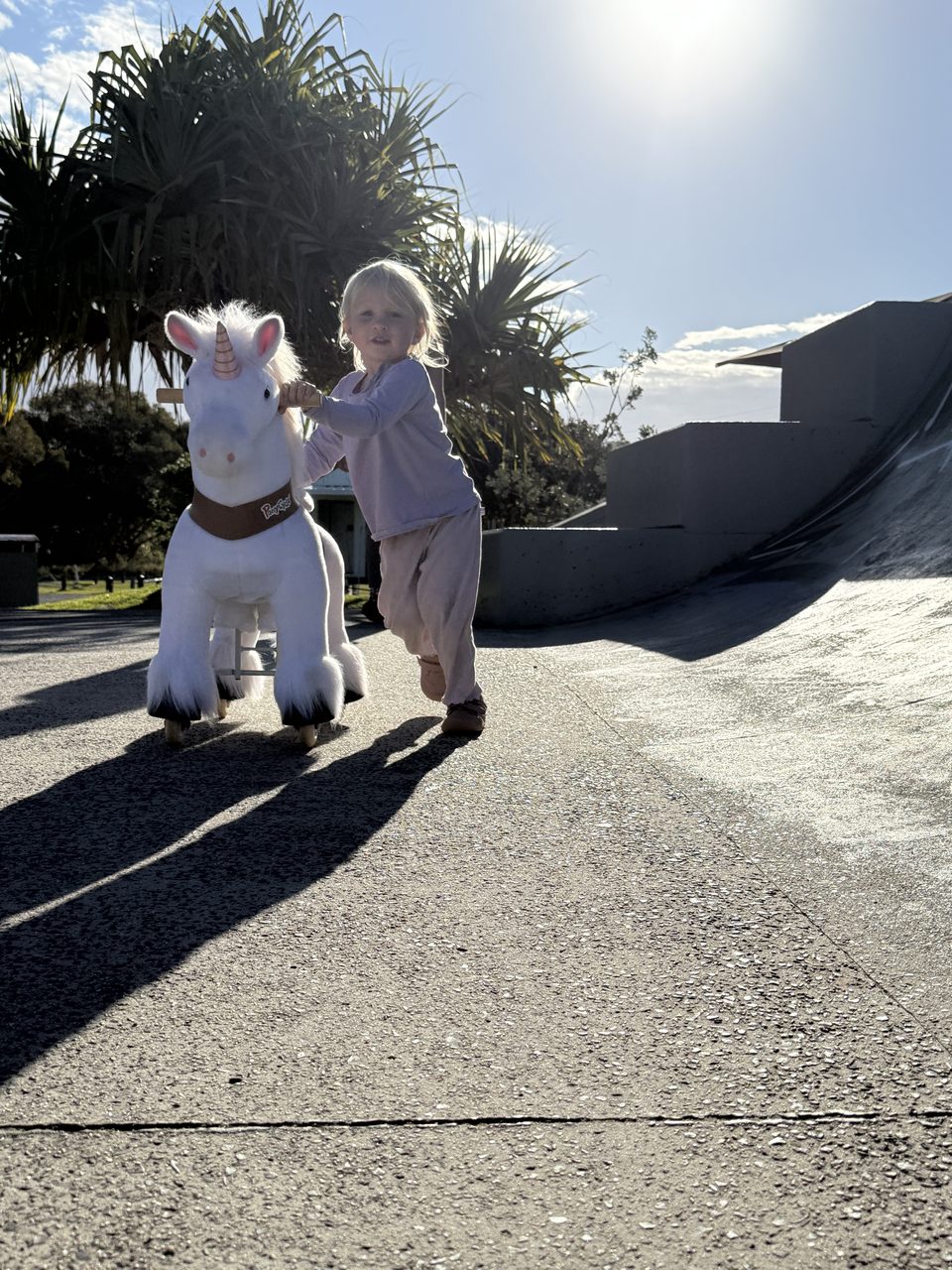 Linnea schiebt ihr weißes Spielzeug-Einhorn im Gegenlicht über den Beton des Skateparks, neben ihr eine Rampe