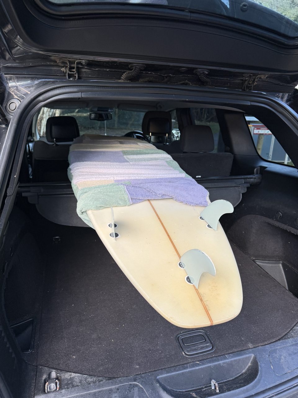 Surfboard liegt bei umgeklappten Rücksitzen längs im Kofferraum des Jeep, in Handtücher gewickelt