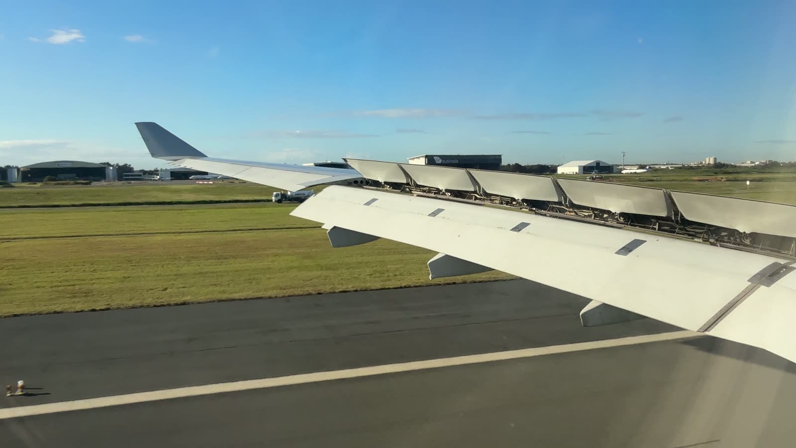 Blick aus dem Flugzeugfenster kurz nach dem Aufsetzen in Brisbane: Tragfläche mit ausgefahrenen Störklappen über dem Rollfeld im Morgenlicht